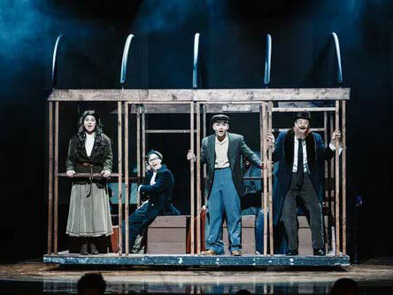 Four actors in a wooden streetcar-like framework on stage in period costumes.