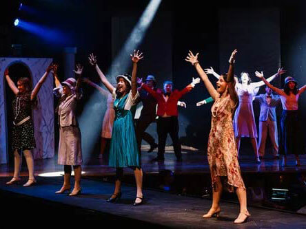 Performers on stage wearing vintage costumes, lit by colorful stage lights.