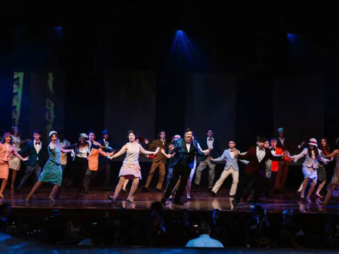 Performers in retro costumes dance on a stage with dramatic blue lighting.