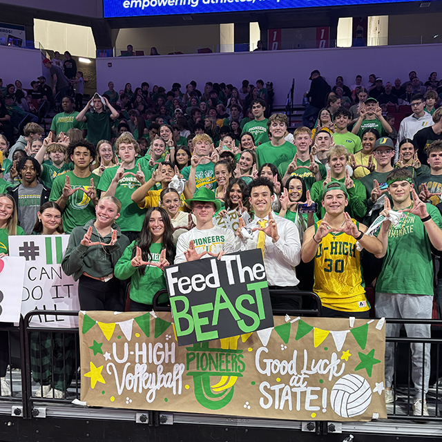 large group of U-high students posing together in a stadium-like setting, at an indoor sports event.